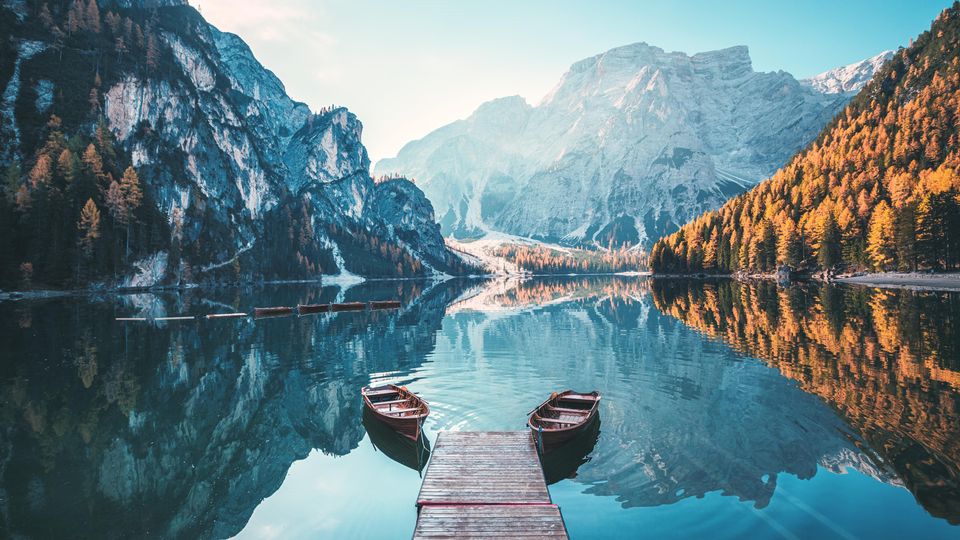 A picture of a mountainside lake, with two boats anchored to a short wooden dock, with mountains in the background